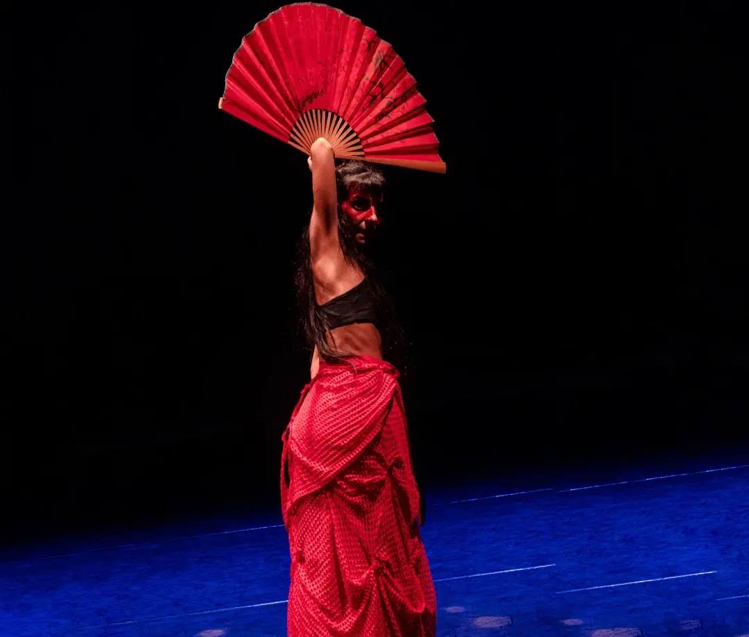 Mulher em apresentação de dança em palco de teatro com saia longa vermelha e leque vermelho